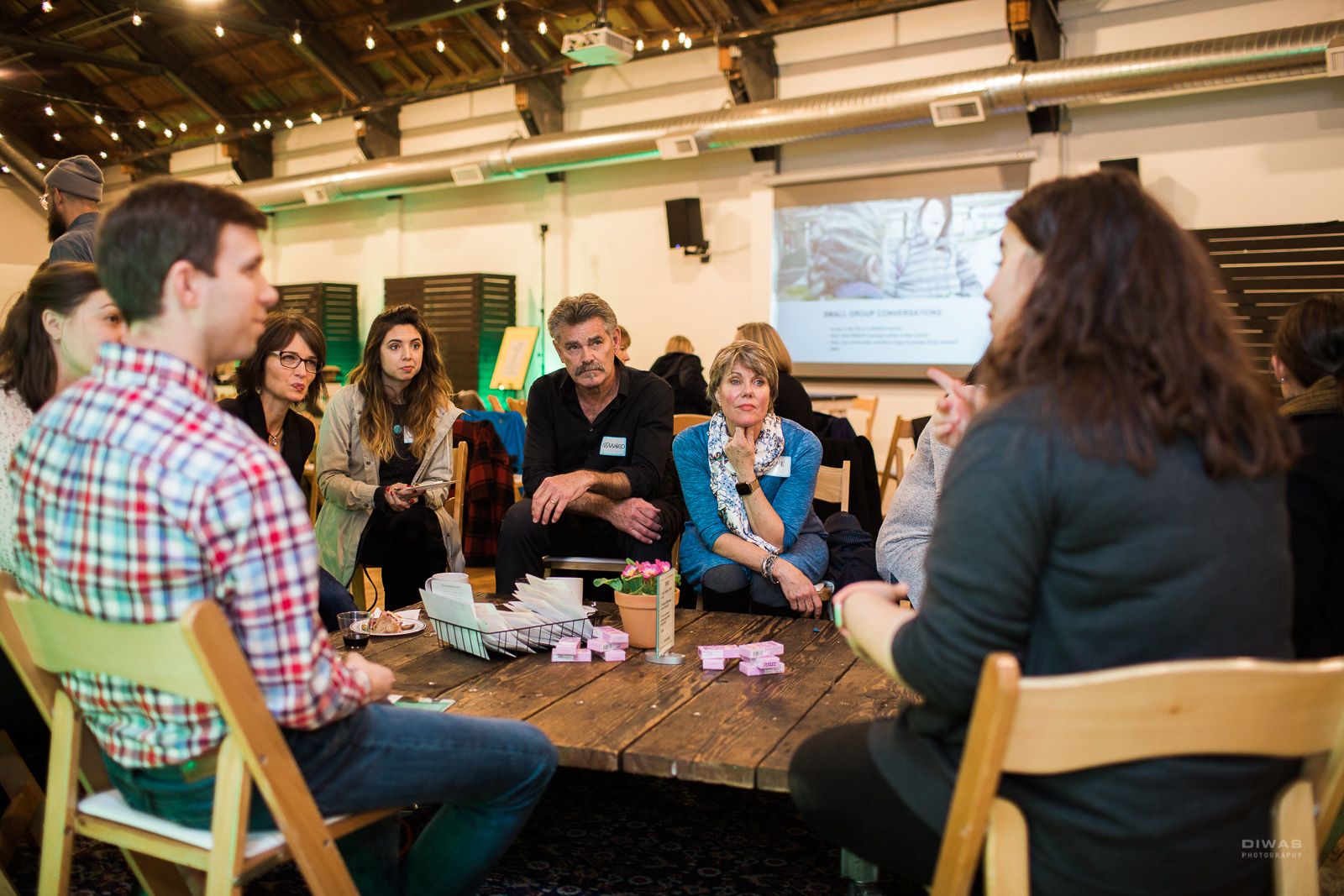 A group of light-skinned people, both from Metropolist and Evergreen Treatment Services, gathered around a table focused on one person as they speak.