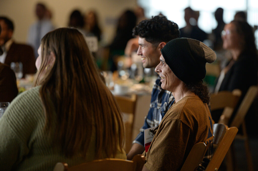 David Delgado is a member of the REACH team. He sits, profile facing the camera, at his table watching the people in stage.