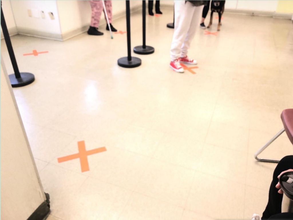 A white tile floor with orange X's on them to indicate where people can wait on a line at six feet apart.