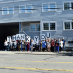 People stand outside of a building holding up letters that read out THANK YOU.