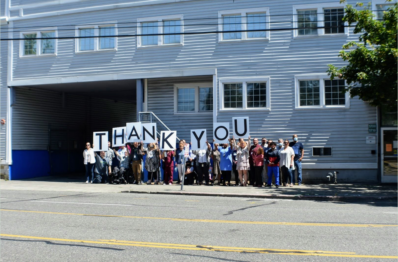 People stand outside of a building holding up letters that read out THANK YOU.